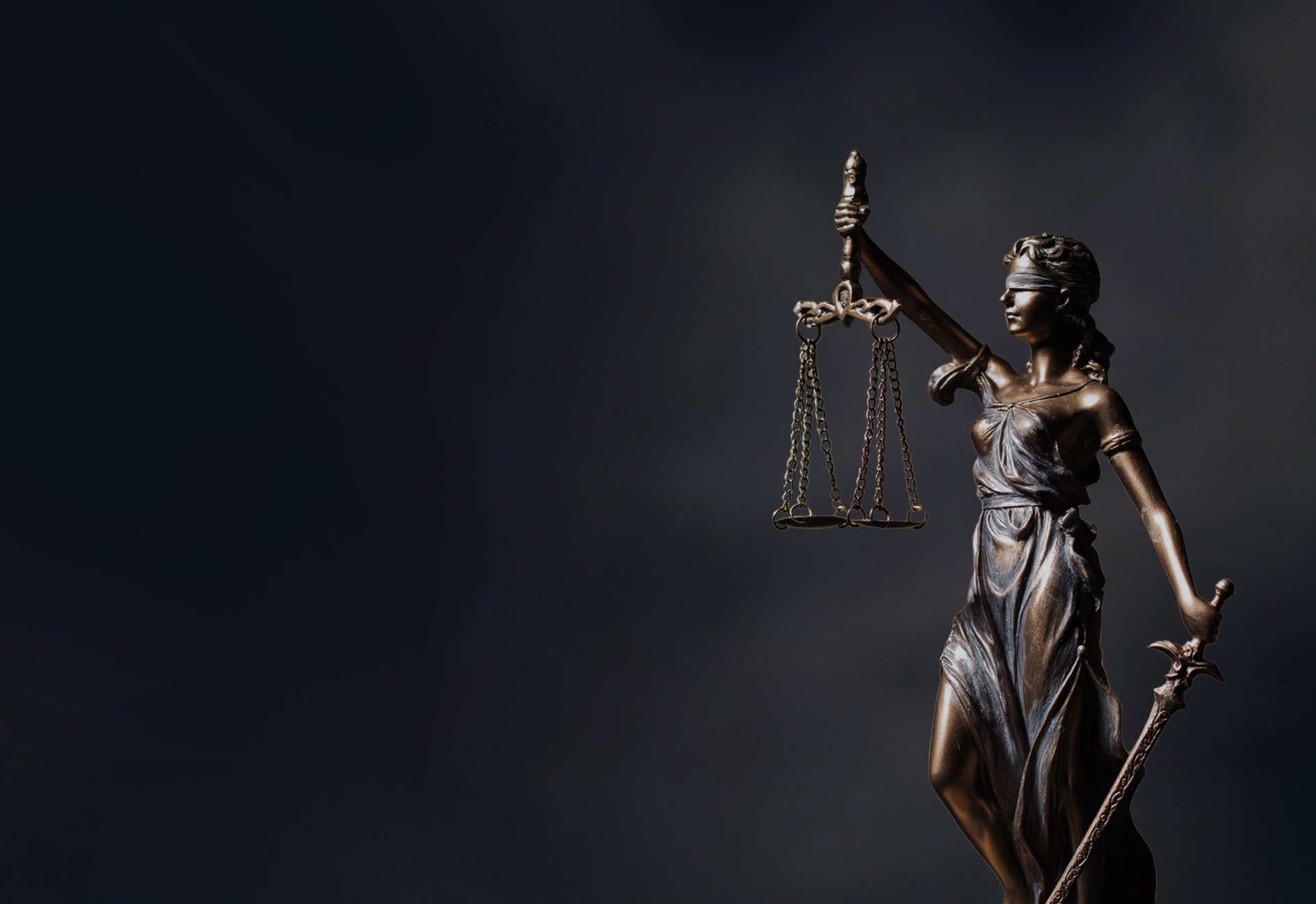Bronze statue of Lady Justice, blindfolded, holding scales and a sword, symbolizing fairness and law, set against a dark background.