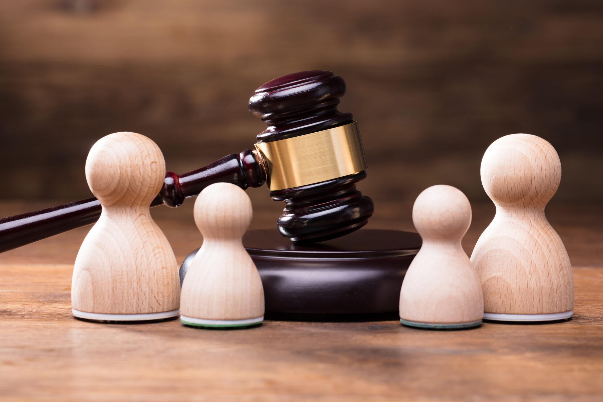 A gavel rests on a wooden block, surrounded by various wooden figurines, symbolizing justice and decision-making in legal contexts.